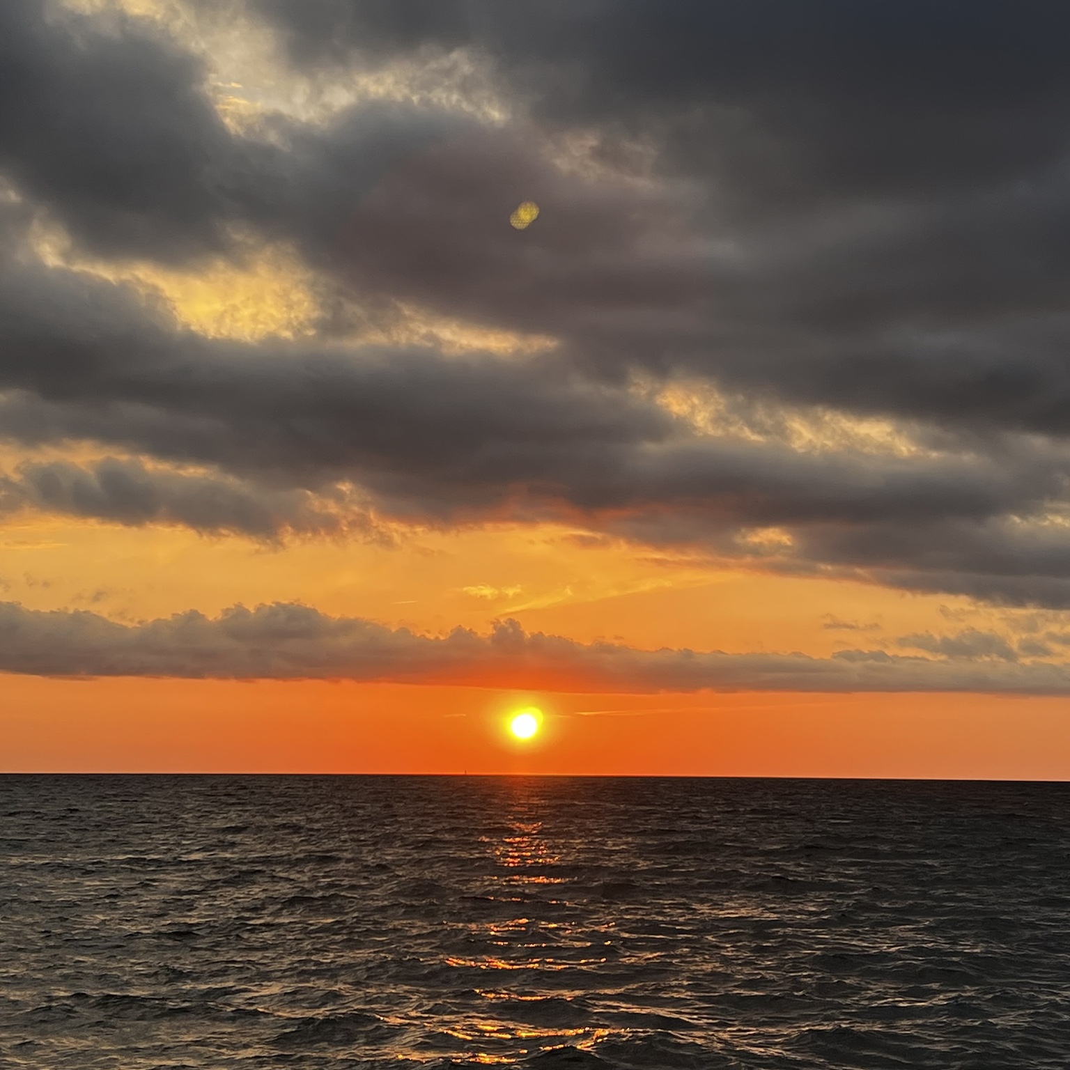 Le soleil à l’horizon au-dessus de la mer sous un ciel nuageux aux couleurs orangées